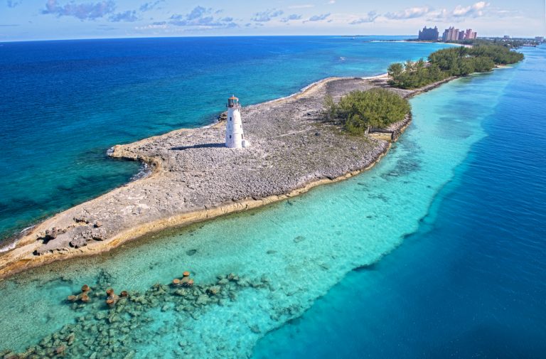 Scenic view of a lighthouse on Paradise Island with clear turquoise waters and nearby resorts.